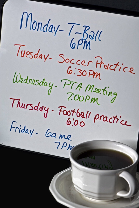A weekly schedule on a white board next to a cup of coffee.