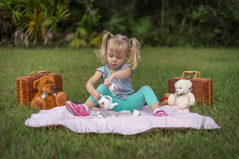 A toddler having a picnic with her teddy bears.