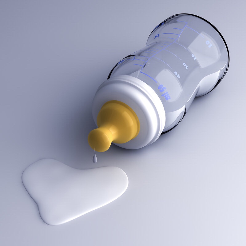 Baby bottle with a heart shaped drop of milk on the floor.