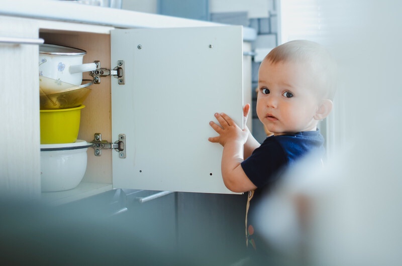 Baby opening cupboards with dishes and pans inside.