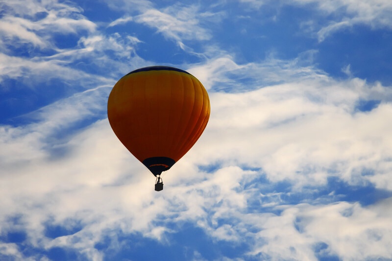 Balloon floating up into a blue sky with clouds.