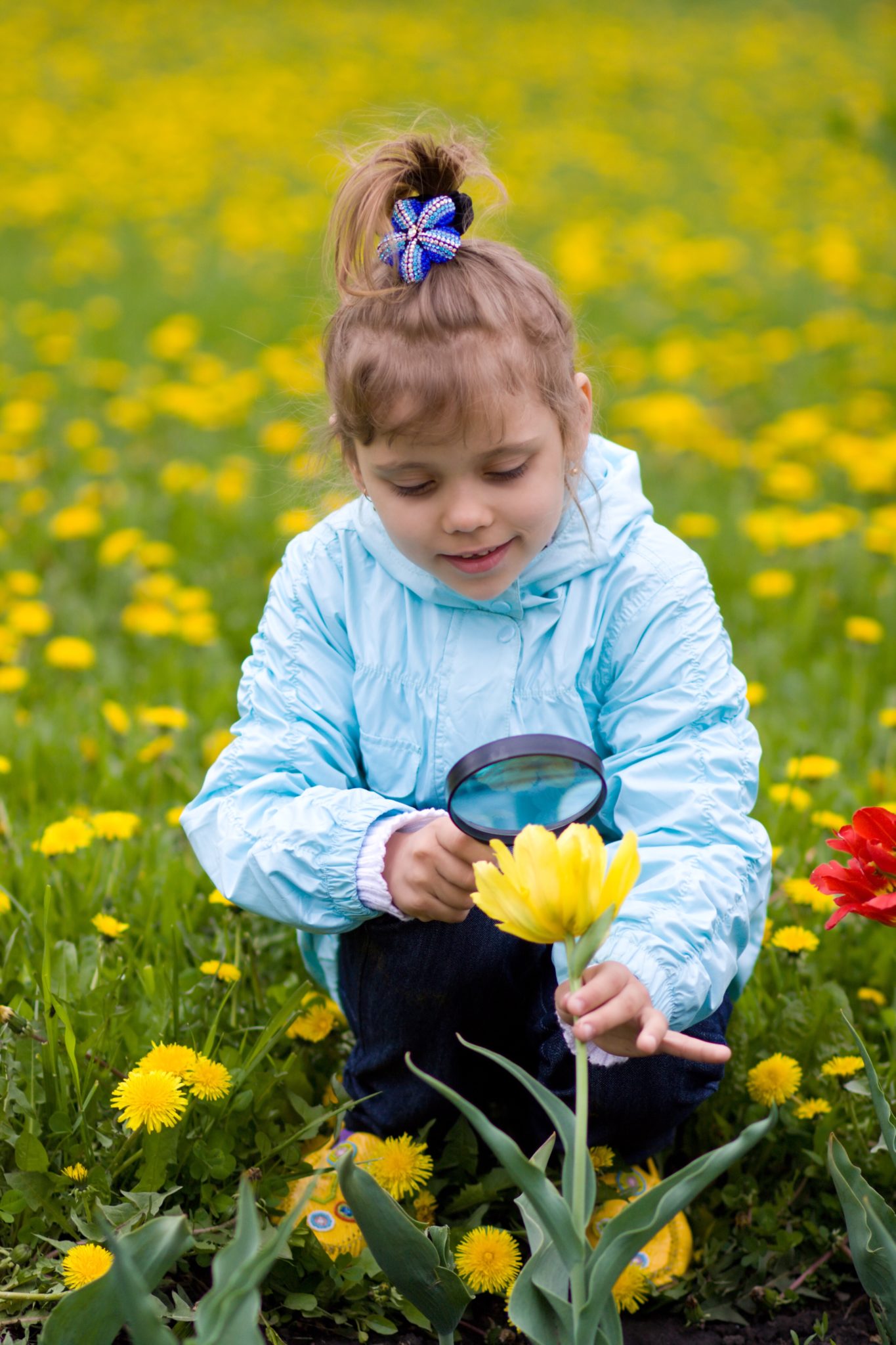 Girl looking at flower through magnifying glass.