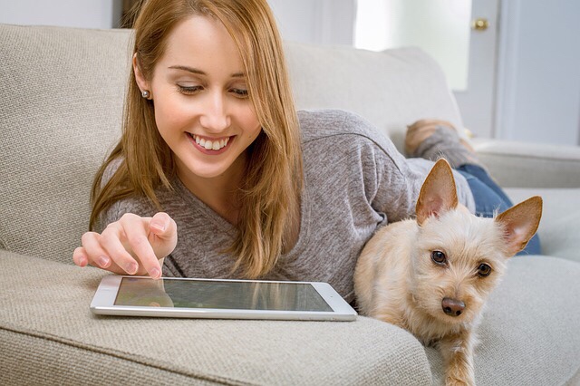 Woman using tablet relaxing next to her dog.