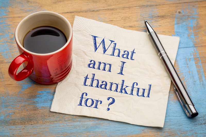 A coffee cup next to a napkin with text, what am I thankful for?