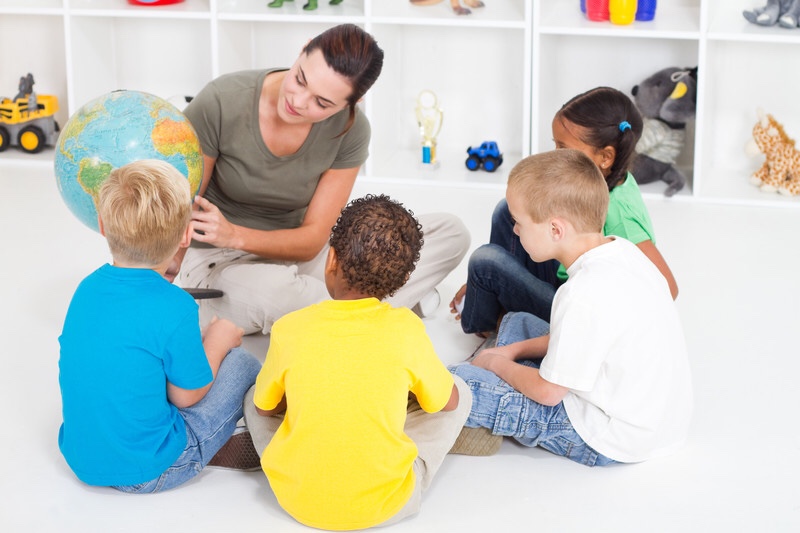 A teacher and multi racial children learning about the globe