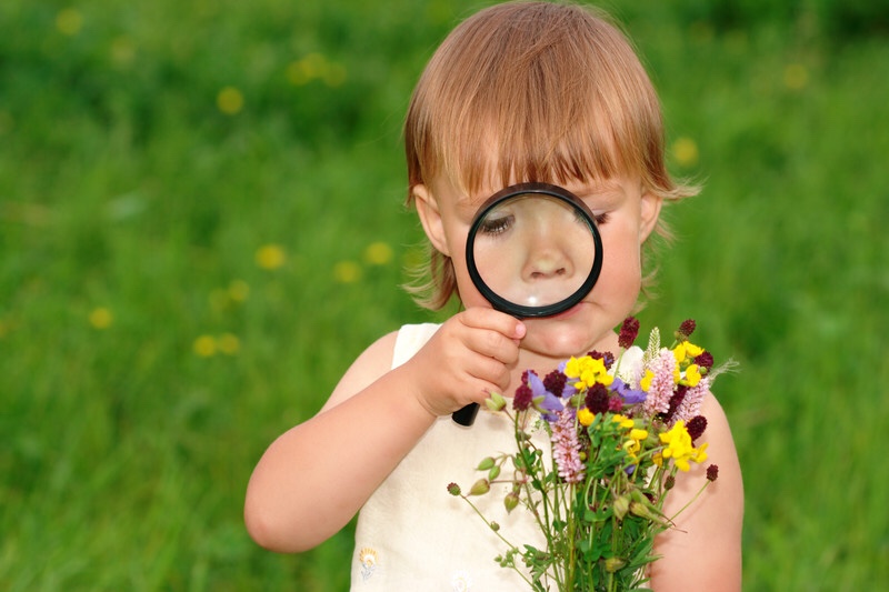 Girl looking at flowers through magnifying glass. Curiosity and discovery.