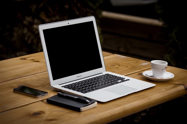 A mac book on a desk next to a cup of coffee.