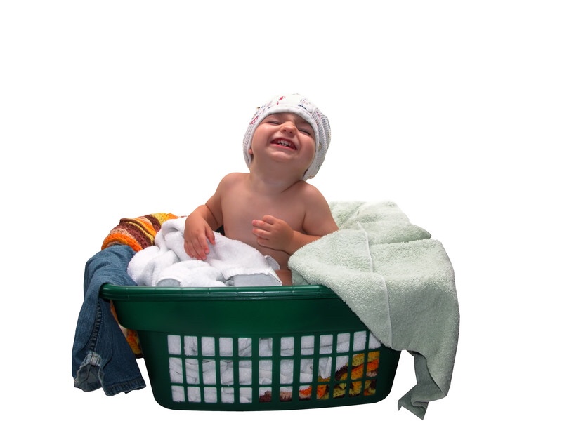 Proud toddler sitting in a laundry basket wearing training pants on his head.