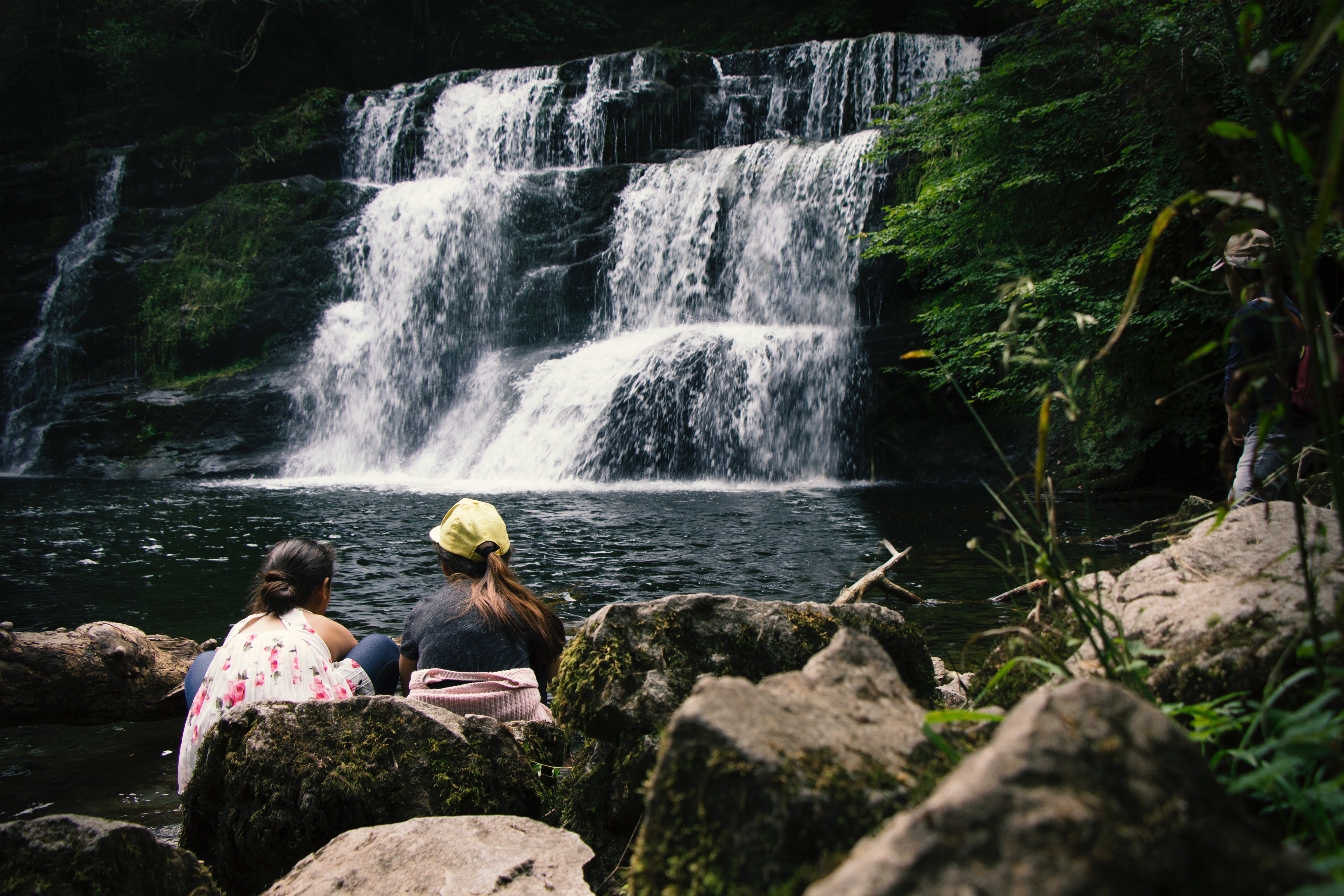 Two women sit in front of waterfall