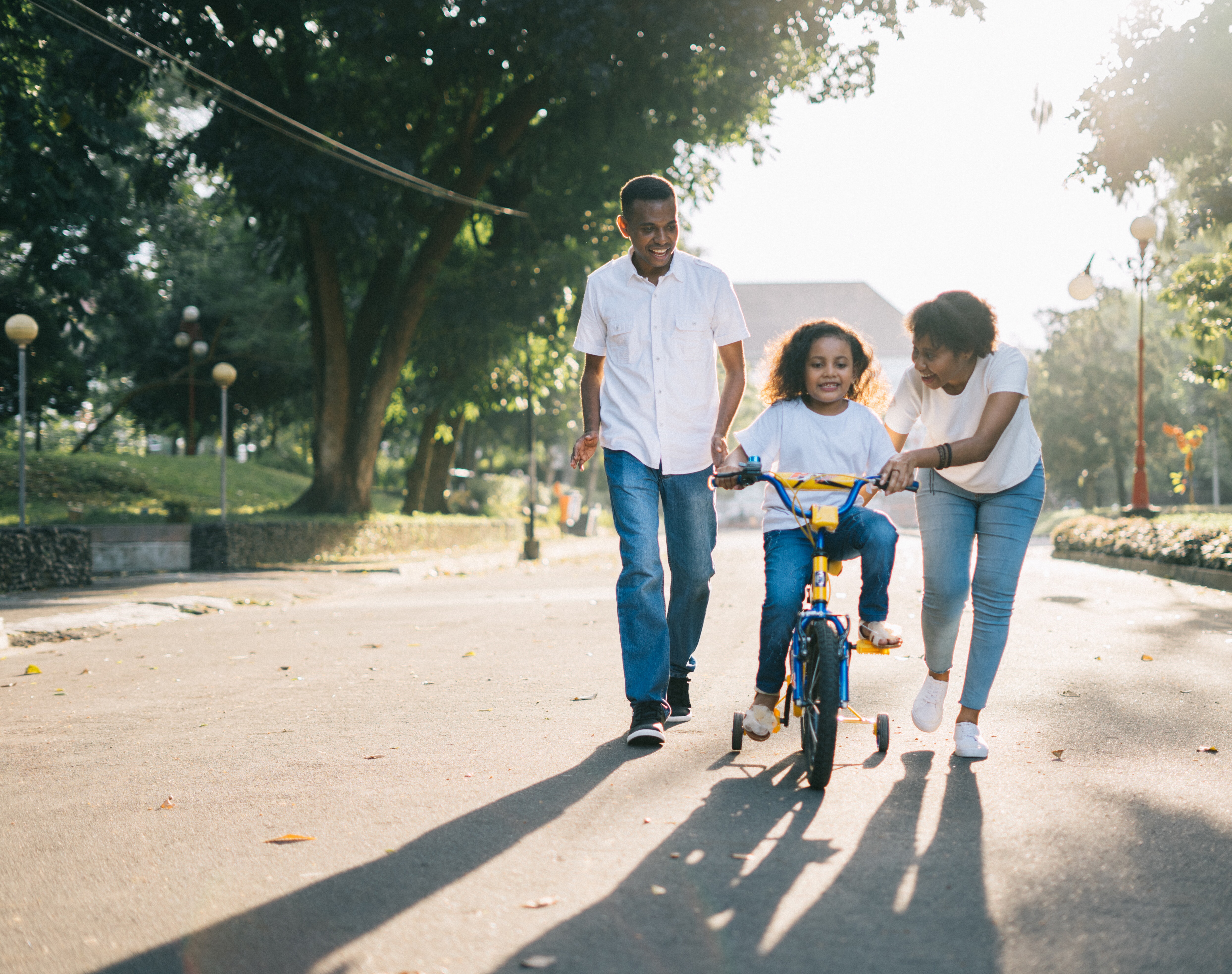 Father teaches child to ride bike while the mother stands next to them.