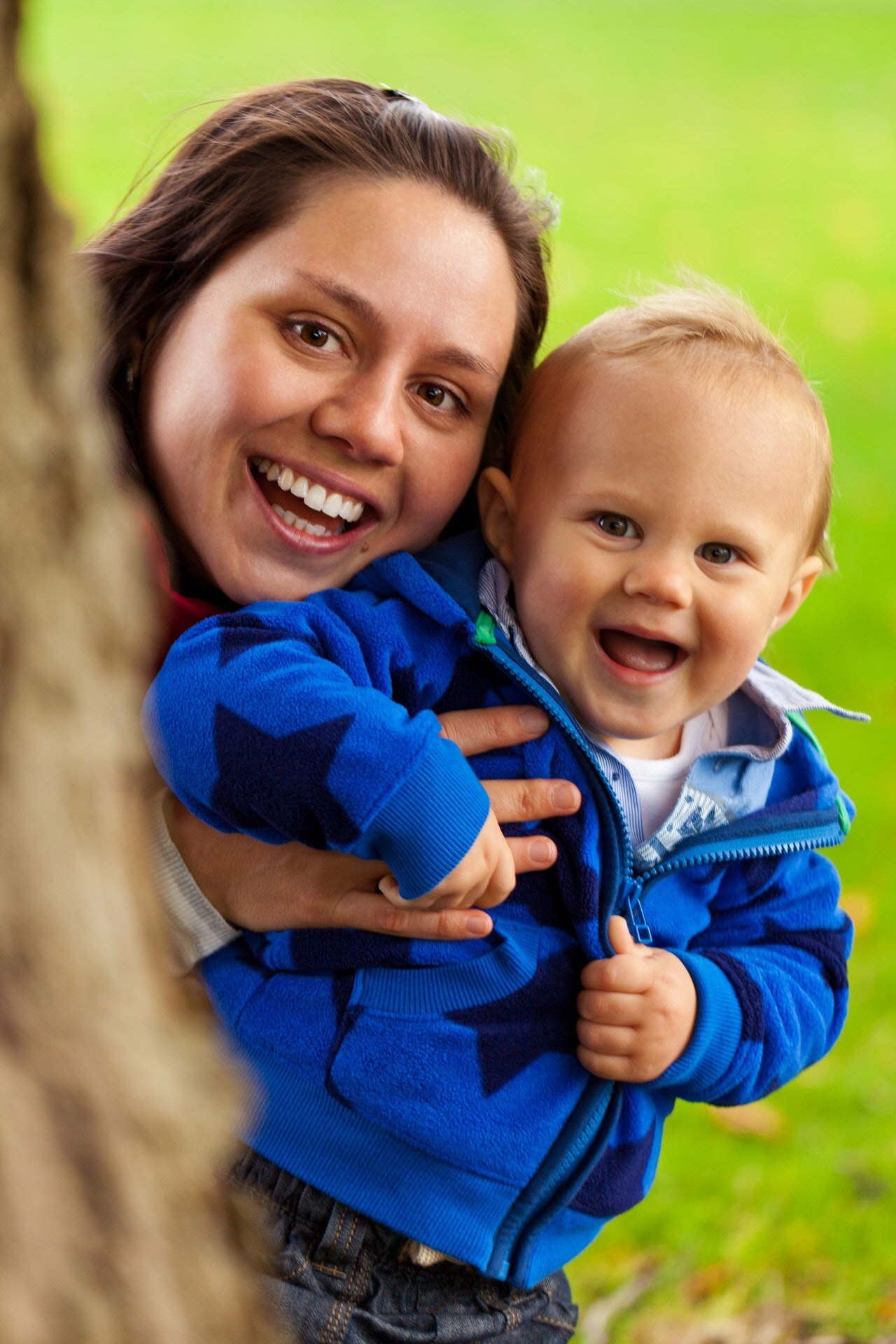 Mother holding baby behind tree trunk