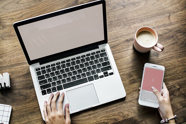 A phone and cup of coffee next to a laptop.