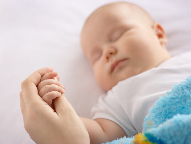 Sleeping baby holding mother’s hand.
