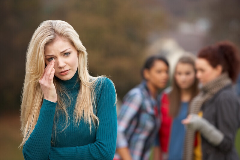 Upset girl standing away from group of gossuping friends.