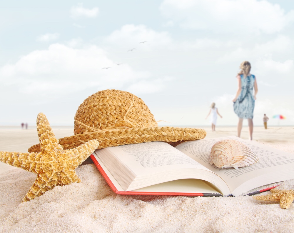 Sea shells, a hat and a book on a beach