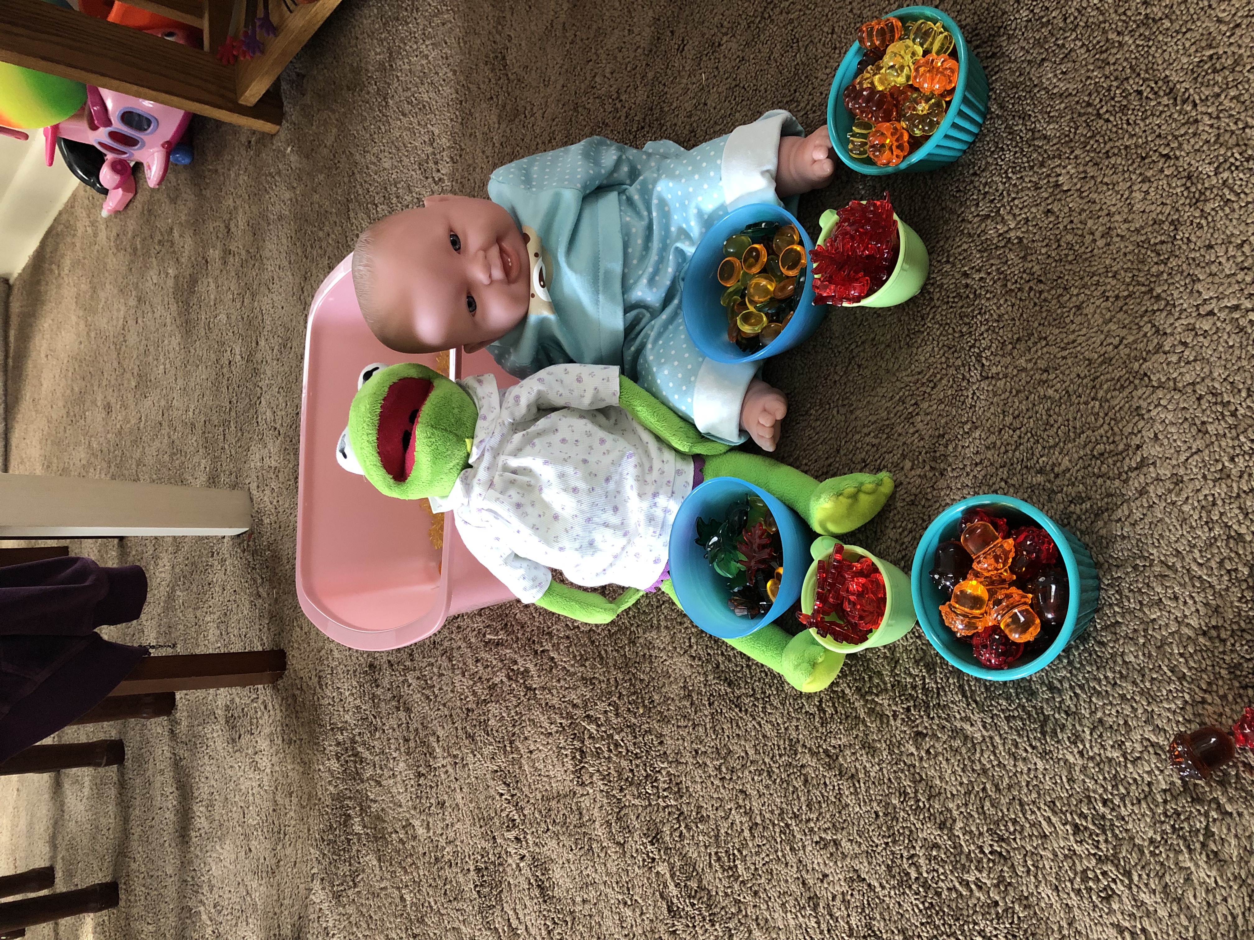 A baby doll and Kermit with bowls of Halloween items.