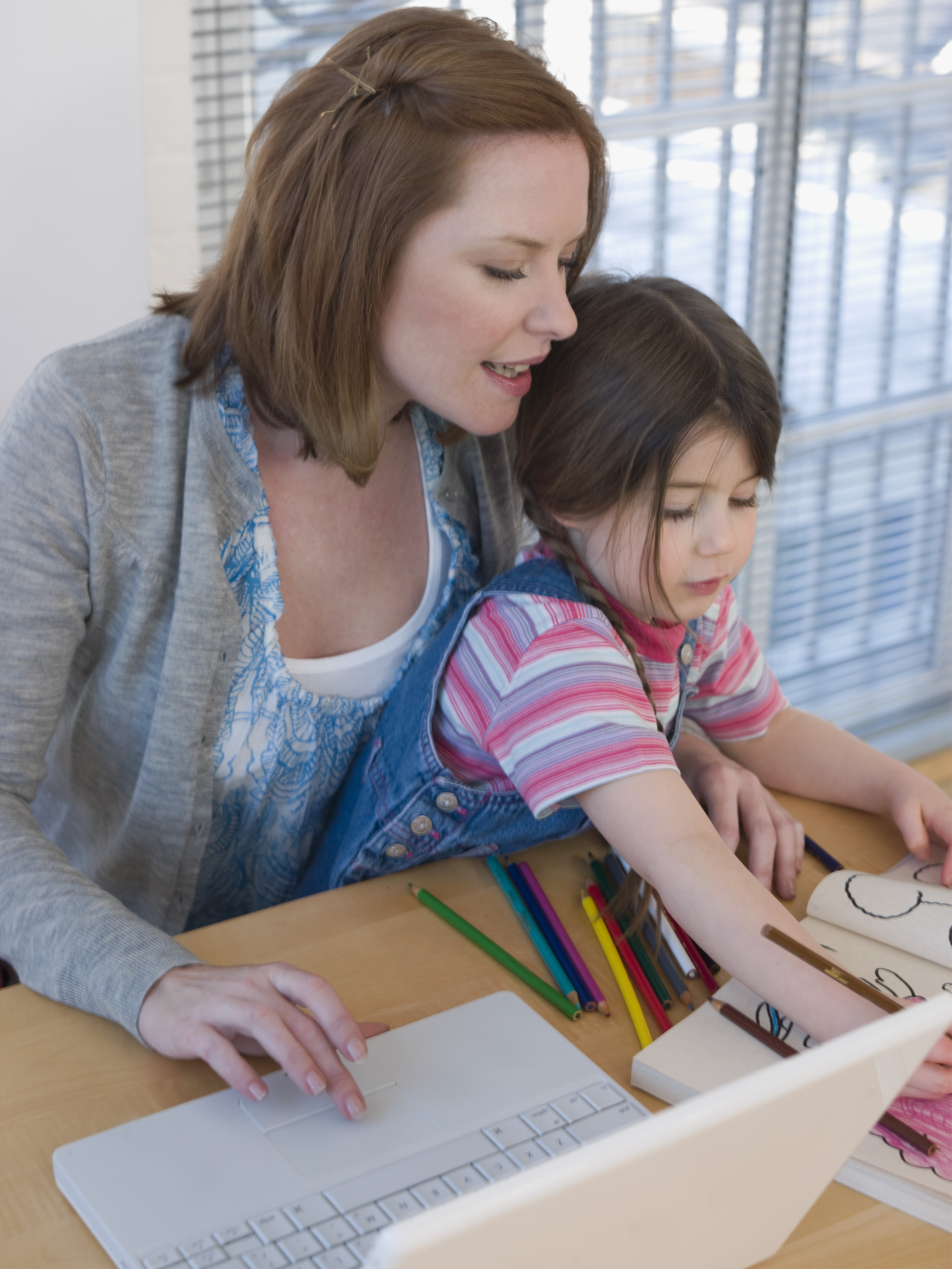 Mother using laptop while daughter colors