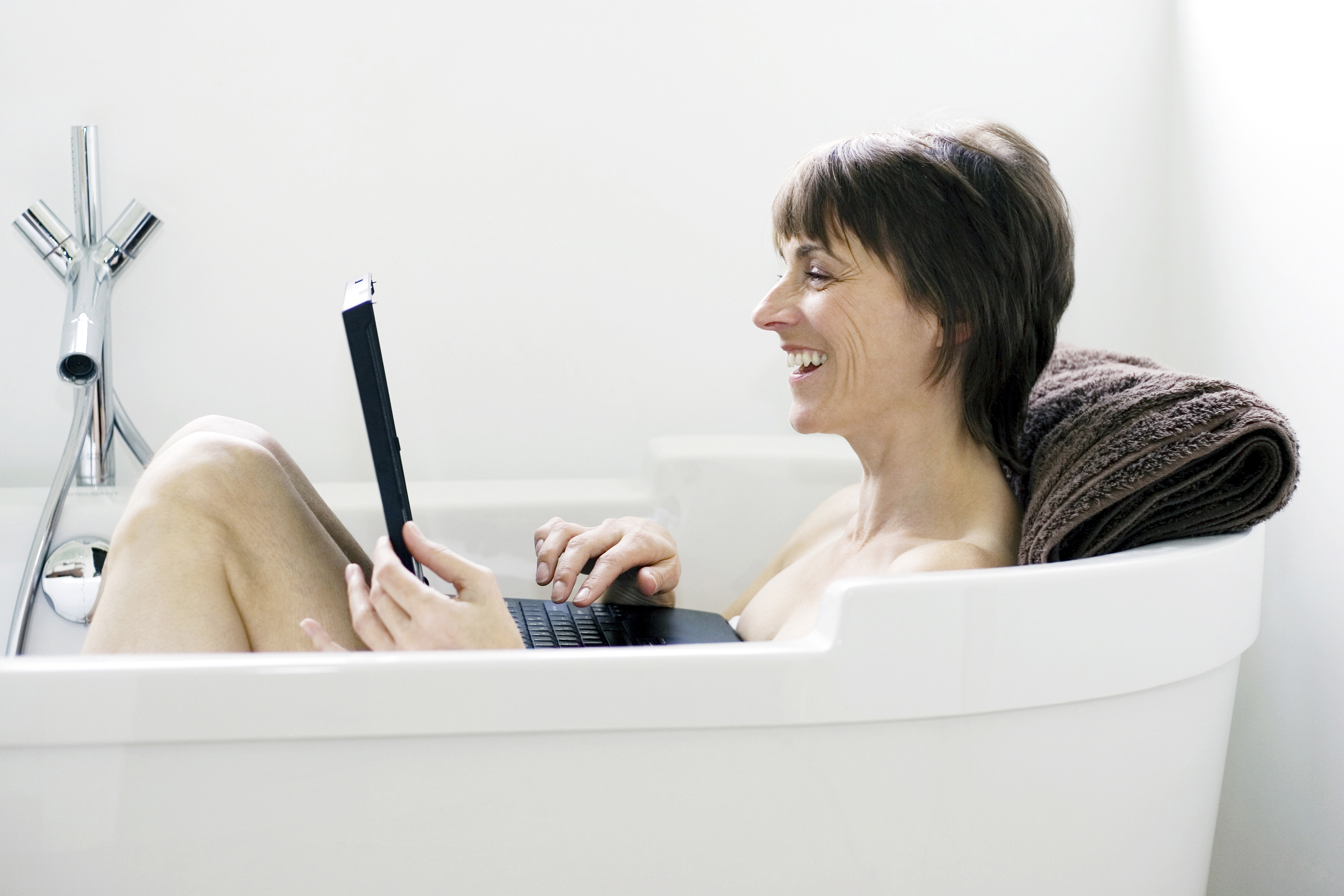 Woman using laptop in a bathtub