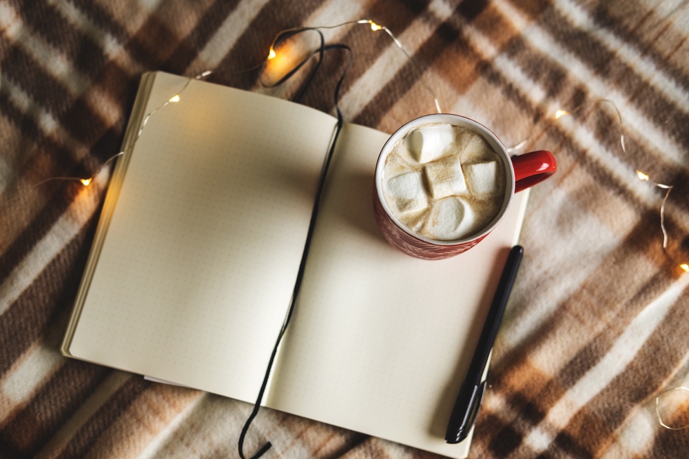 A cozy winter place to journal. A mug of hot chocolate next to a notebook.