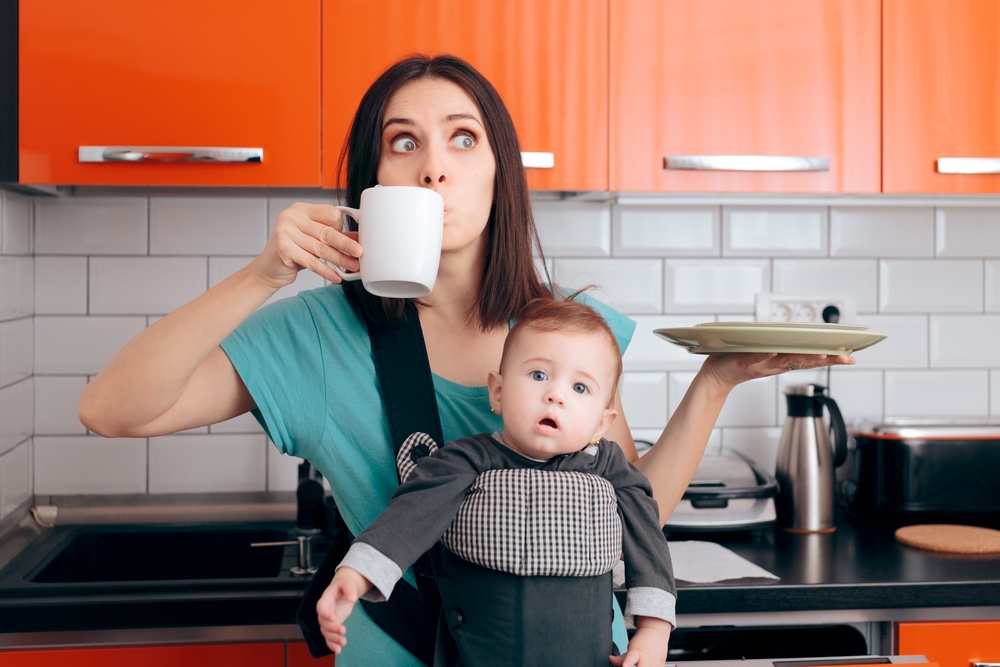 Overwhelmed multitasking mom with dishes, cup of coffee and baby